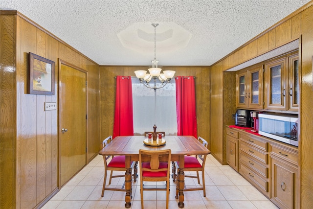 tiled dining space with a textured ceiling, wooden walls, ornamental molding, and a chandelier