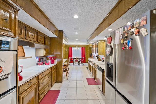 kitchen with appliances with stainless steel finishes, decorative light fixtures, a chandelier, light tile patterned floors, and a textured ceiling