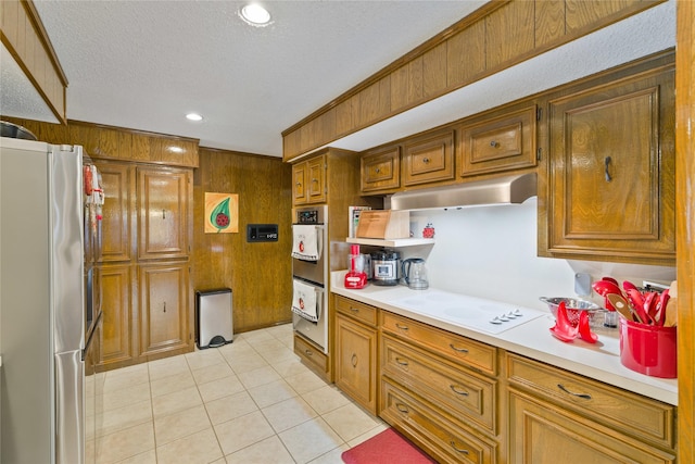 kitchen with wooden walls, under cabinet range hood, light countertops, brown cabinetry, and stainless steel appliances