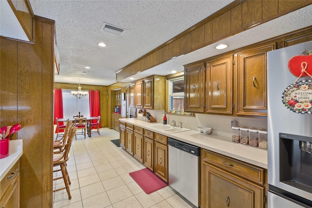 kitchen featuring sink, appliances with stainless steel finishes, a textured ceiling, decorative light fixtures, and wood walls