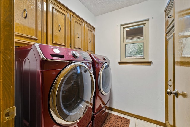 laundry area featuring a textured ceiling, cabinet space, light tile patterned flooring, baseboards, and washing machine and clothes dryer