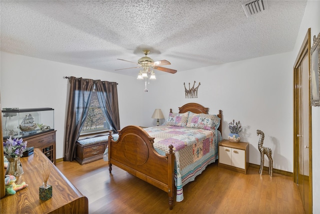 bedroom with visible vents, baseboards, ceiling fan, wood finished floors, and a textured ceiling