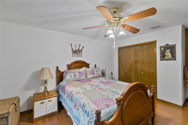 bedroom with visible vents, a textured ceiling, wood finished floors, a closet, and ceiling fan