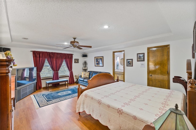 bedroom with visible vents, a raised ceiling, a textured ceiling, and wood finished floors