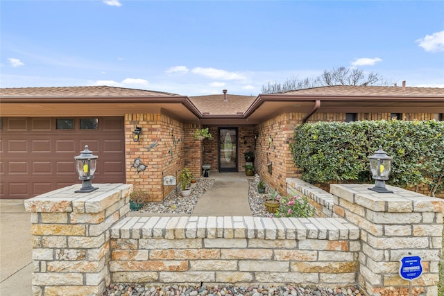 entrance to property featuring an attached garage, brick siding, and a shingled roof