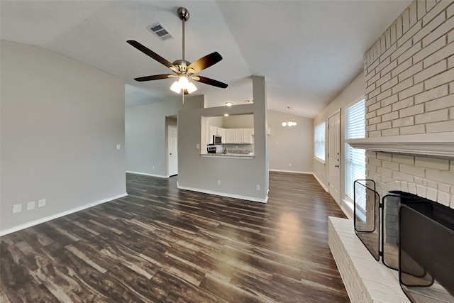 unfurnished living room featuring ceiling fan with notable chandelier, lofted ceiling, a fireplace, and dark hardwood / wood-style floors