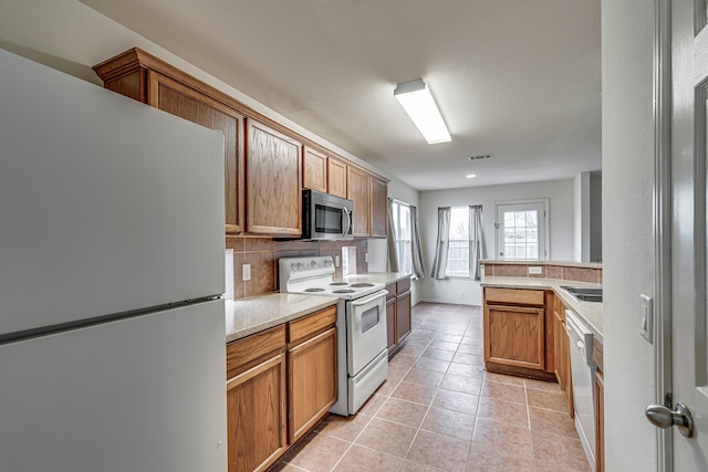 kitchen with tasteful backsplash, light tile patterned floors, and white appliances