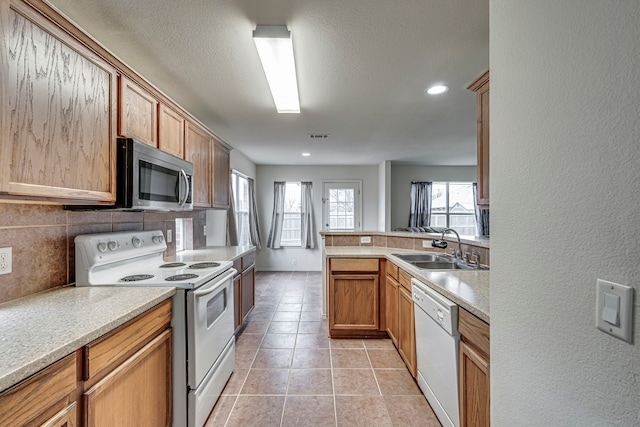 kitchen featuring sink, white appliances, backsplash, light tile patterned flooring, and kitchen peninsula