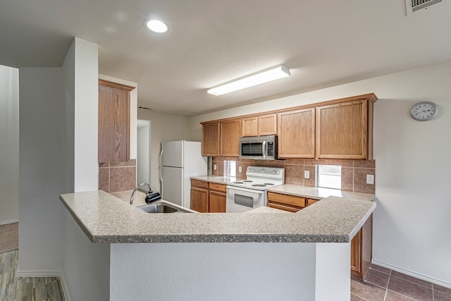 kitchen with sink, backsplash, kitchen peninsula, light stone countertops, and white appliances