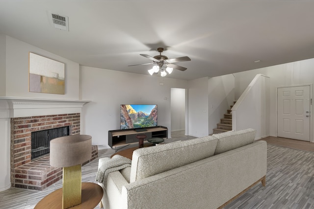 living room featuring wood-type flooring, a brick fireplace, and ceiling fan