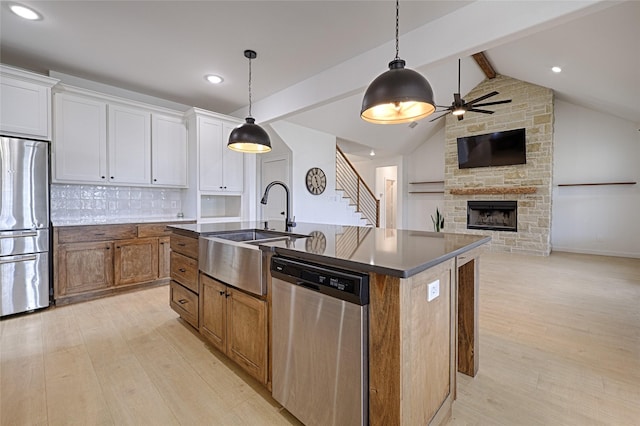 kitchen with white cabinets, appliances with stainless steel finishes, decorative backsplash, hanging light fixtures, and a kitchen island with sink