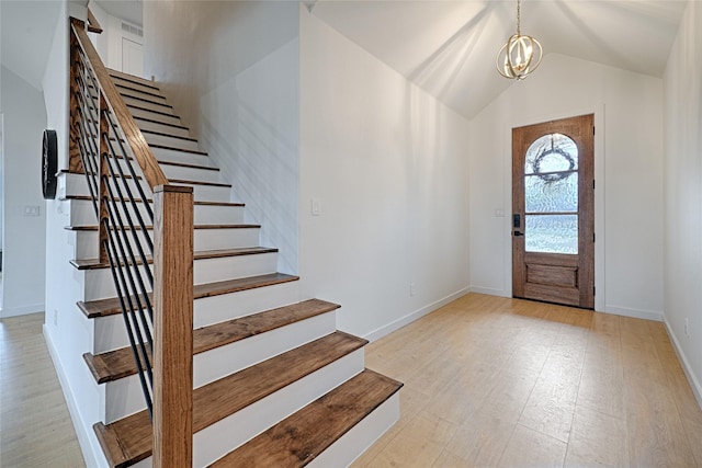 foyer entrance featuring vaulted ceiling, an inviting chandelier, and light hardwood / wood-style flooring