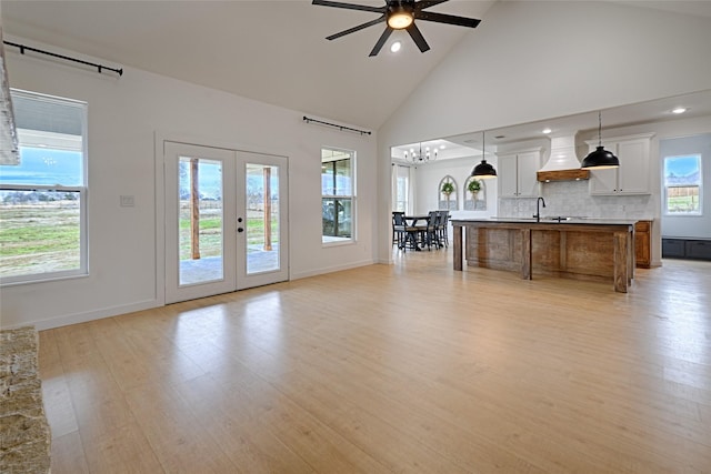 unfurnished living room with light hardwood / wood-style floors, high vaulted ceiling, french doors, and ceiling fan with notable chandelier