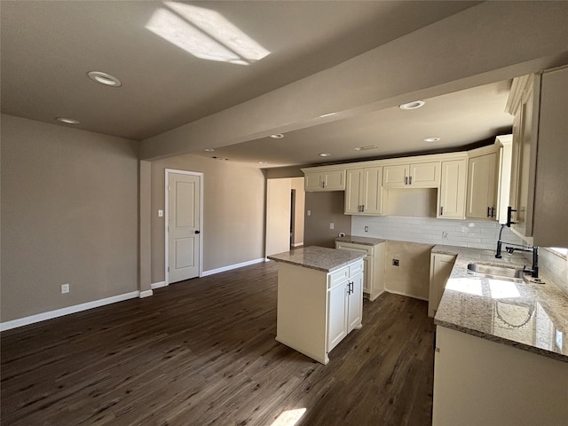 kitchen with decorative backsplash, dark hardwood / wood-style flooring, light stone countertops, a kitchen island, and sink