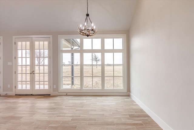 interior space with french doors, a notable chandelier, vaulted ceiling, and light hardwood / wood-style floors