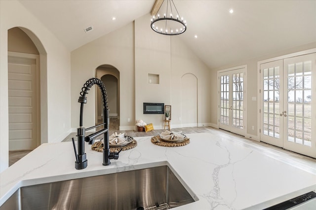 kitchen featuring light stone countertops, pendant lighting, french doors, sink, and a notable chandelier