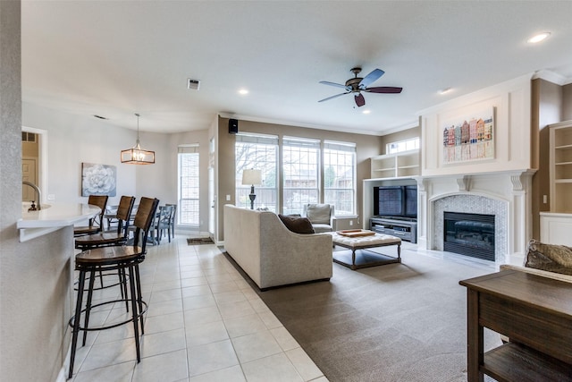 tiled living room featuring ceiling fan, ornamental molding, a tile fireplace, and sink