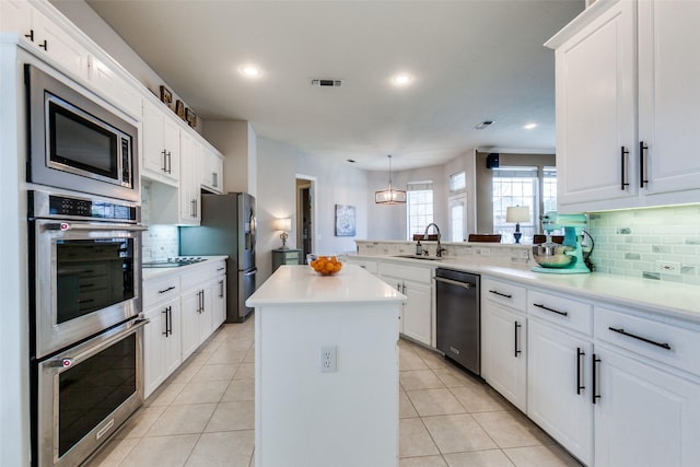 kitchen featuring a kitchen island, white cabinetry, stainless steel appliances, sink, and kitchen peninsula