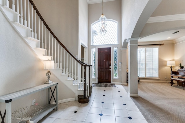 carpeted foyer featuring an inviting chandelier, crown molding, a towering ceiling, and decorative columns