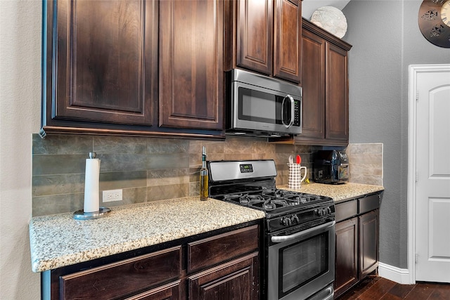 kitchen featuring dark brown cabinetry, stainless steel appliances, decorative backsplash, dark hardwood / wood-style floors, and light stone counters