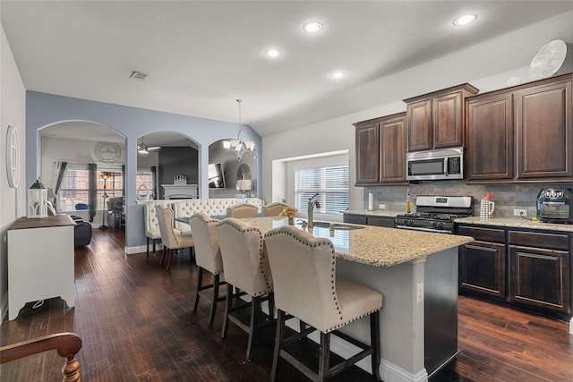 kitchen featuring pendant lighting, a kitchen island with sink, dark brown cabinets, stainless steel appliances, and decorative backsplash