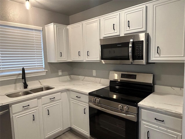 kitchen with light stone countertops, white cabinets, appliances with stainless steel finishes, and sink