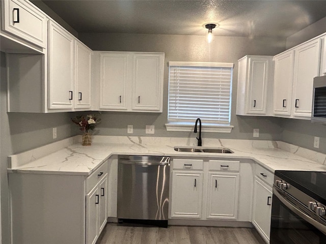 kitchen with light hardwood / wood-style floors, sink, white cabinetry, appliances with stainless steel finishes, and light stone counters