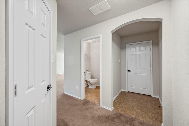 hallway featuring arched walkways, carpet, visible vents, and baseboards