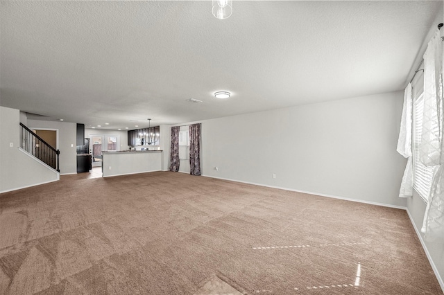 unfurnished living room with baseboards, an inviting chandelier, stairs, a textured ceiling, and carpet floors