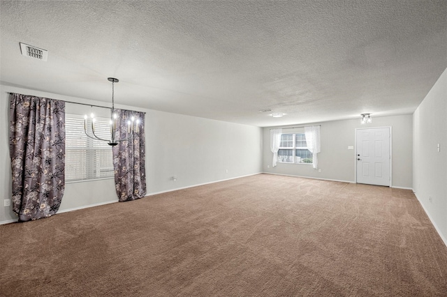 spare room with light colored carpet, visible vents, a textured ceiling, a chandelier, and baseboards