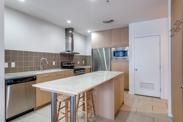 kitchen with wall chimney range hood, a center island, a kitchen bar, sink, and appliances with stainless steel finishes