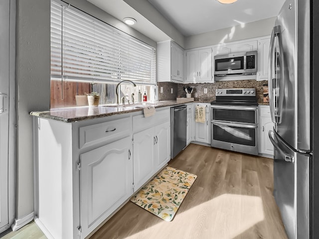 kitchen featuring appliances with stainless steel finishes, sink, white cabinetry, dark stone countertops, and decorative backsplash