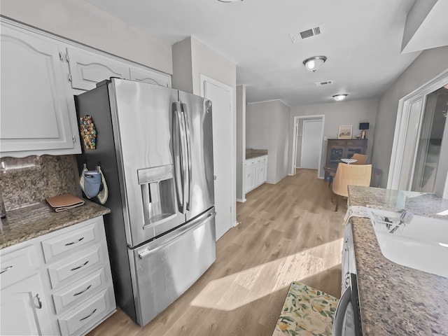 kitchen featuring light wood-type flooring, dark stone counters, white cabinetry, and stainless steel fridge