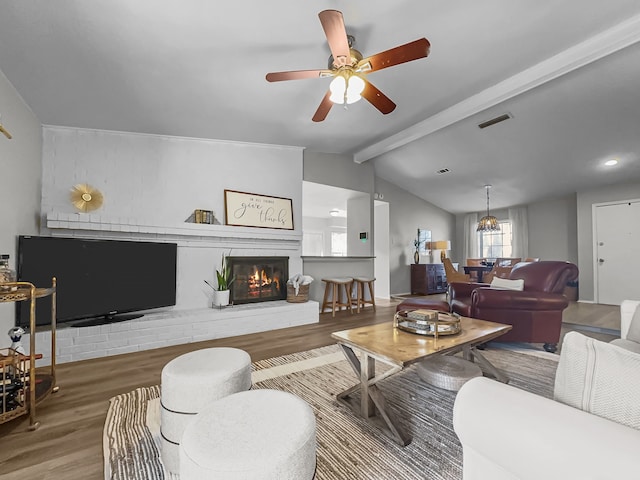 living room featuring ceiling fan, hardwood / wood-style flooring, vaulted ceiling with beams, and a brick fireplace