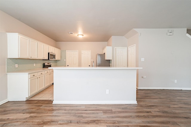 kitchen with a center island with sink, appliances with stainless steel finishes, light hardwood / wood-style floors, and white cabinetry