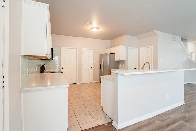 kitchen featuring white cabinets, range, decorative backsplash, stainless steel fridge, and light tile patterned floors