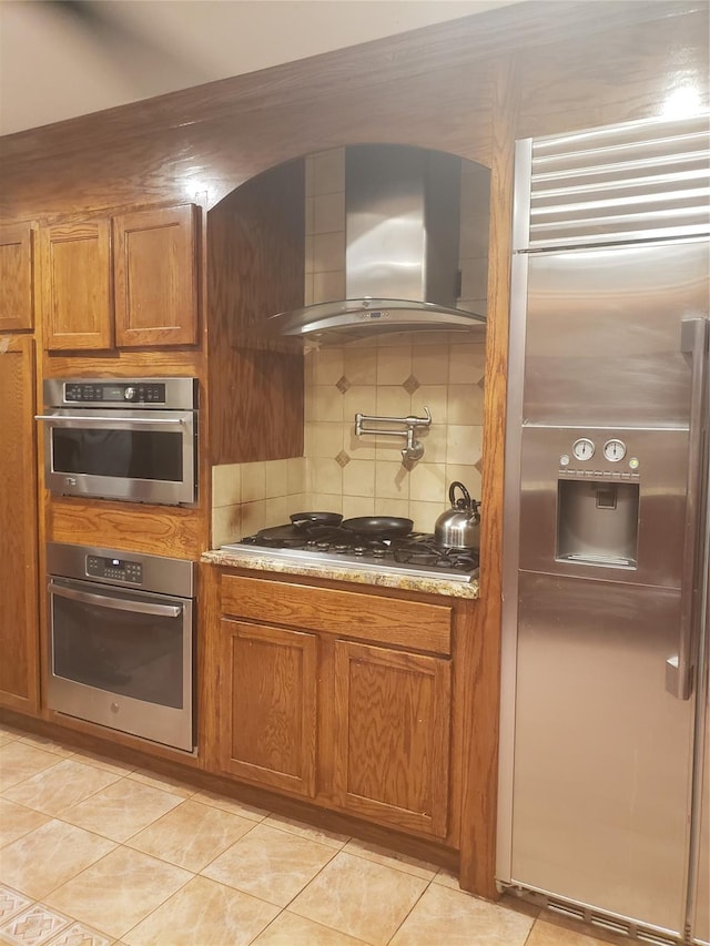 kitchen with light tile patterned floors, backsplash, appliances with stainless steel finishes, and wall chimney exhaust hood