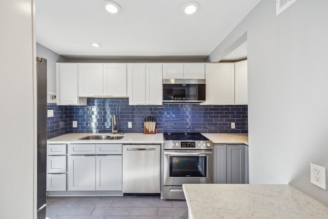 kitchen featuring appliances with stainless steel finishes, sink, white cabinetry, light stone counters, and decorative backsplash