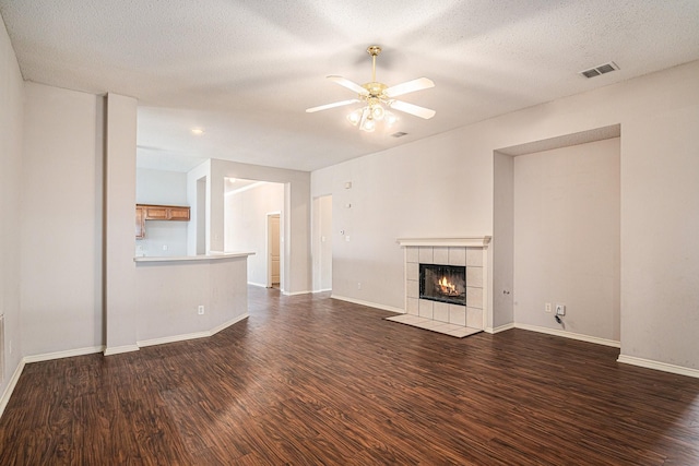 unfurnished living room featuring a tiled fireplace, dark wood-type flooring, a textured ceiling, and ceiling fan