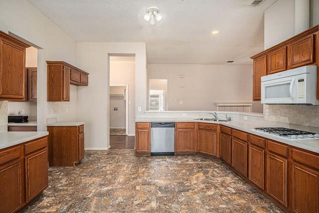 kitchen with tasteful backsplash, sink, white appliances, kitchen peninsula, and a textured ceiling