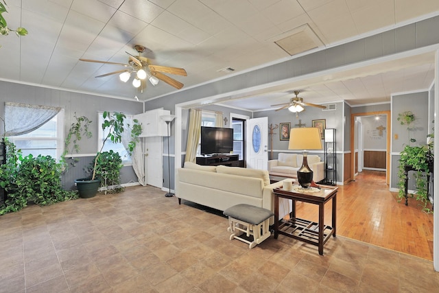 living room featuring ceiling fan, wooden walls, and ornamental molding