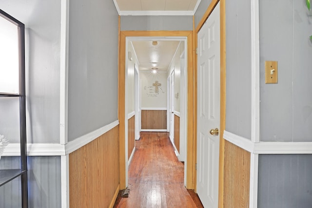 corridor with hardwood / wood-style floors, ornamental molding, a textured ceiling, and wooden walls