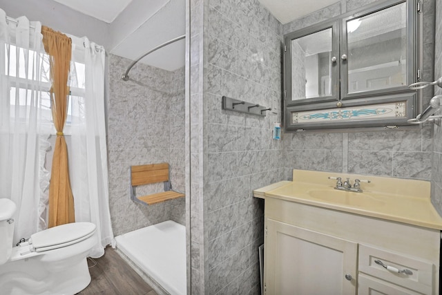 bathroom featuring toilet, a shower, tile walls, wood-type flooring, and vanity