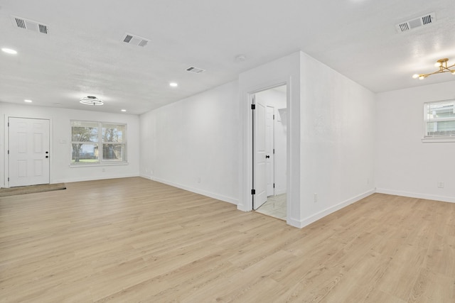 empty room featuring plenty of natural light, light hardwood / wood-style flooring, and an inviting chandelier