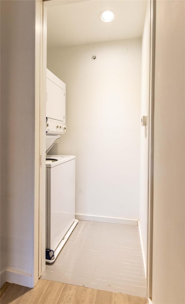 laundry area featuring stacked washer and dryer and light hardwood / wood-style flooring