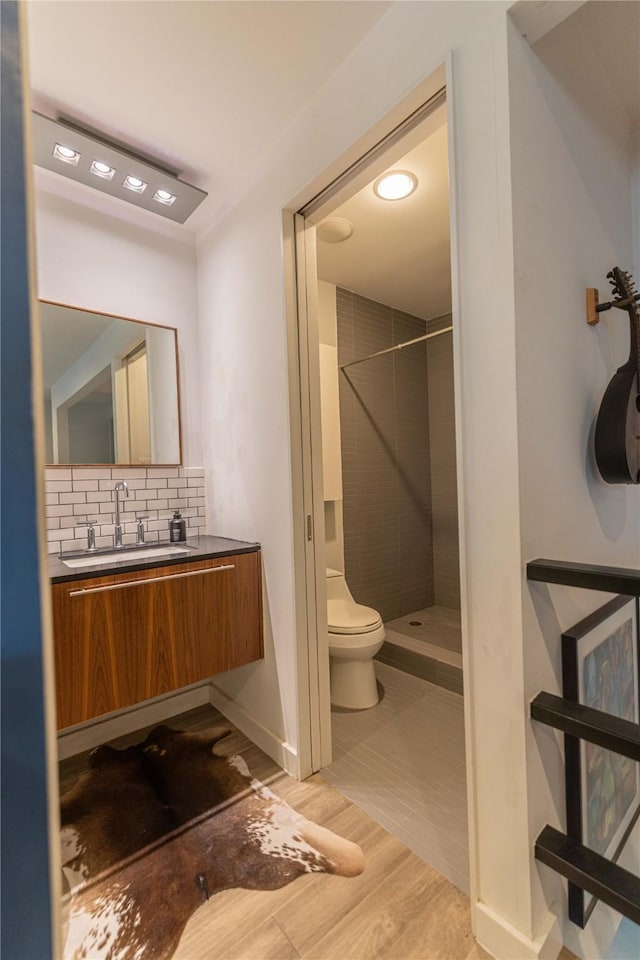 bathroom with toilet, vanity, tiled shower, decorative backsplash, and hardwood / wood-style flooring