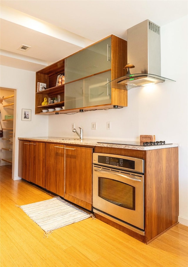 kitchen with stainless steel oven, sink, light hardwood / wood-style flooring, and exhaust hood