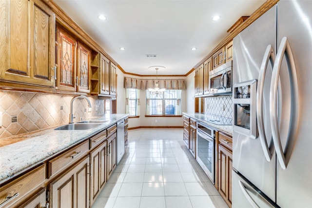 kitchen featuring pendant lighting, sink, crown molding, stainless steel appliances, and light stone counters