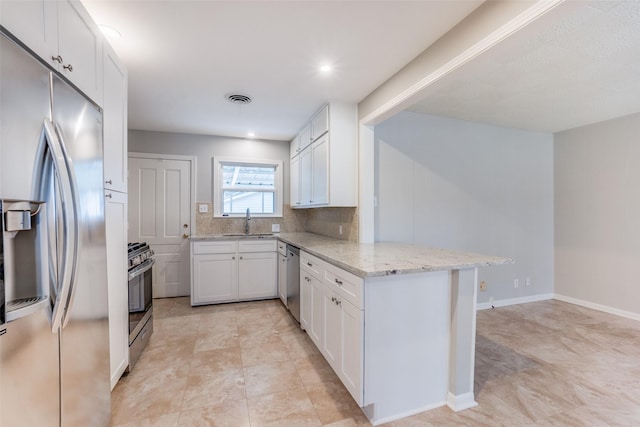 kitchen with kitchen peninsula, sink, white cabinetry, appliances with stainless steel finishes, and light stone counters