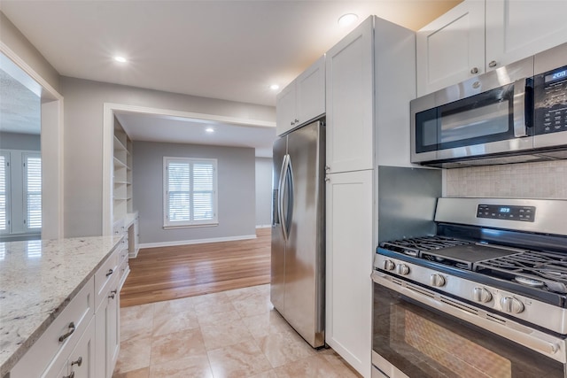 kitchen featuring stainless steel appliances, white cabinetry, and light stone countertops